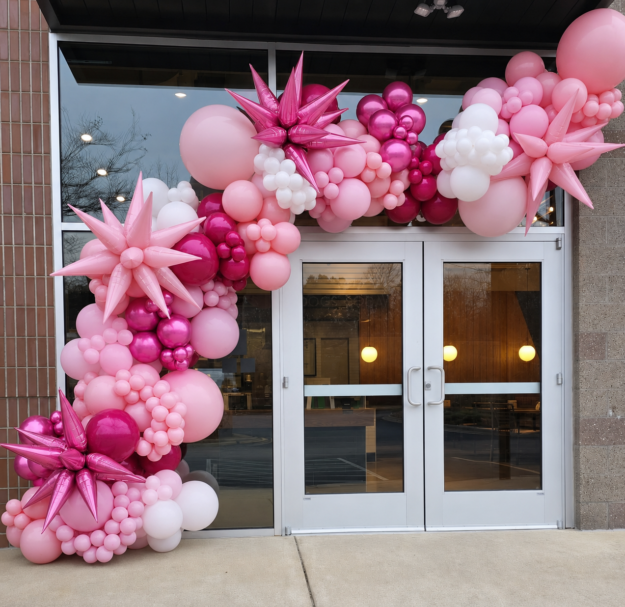 Blush pink balloon garland arch framing a storefront grand opening entrance