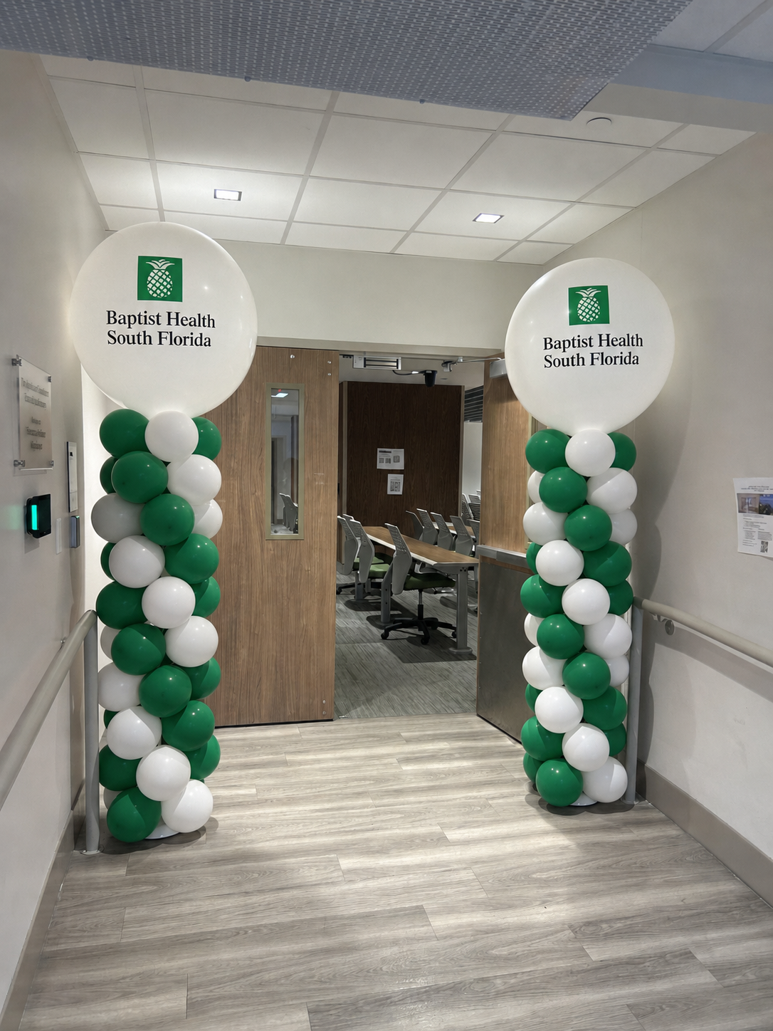 Green and white balloon columns with branded toppers at a Baptist Health South Florida entrance